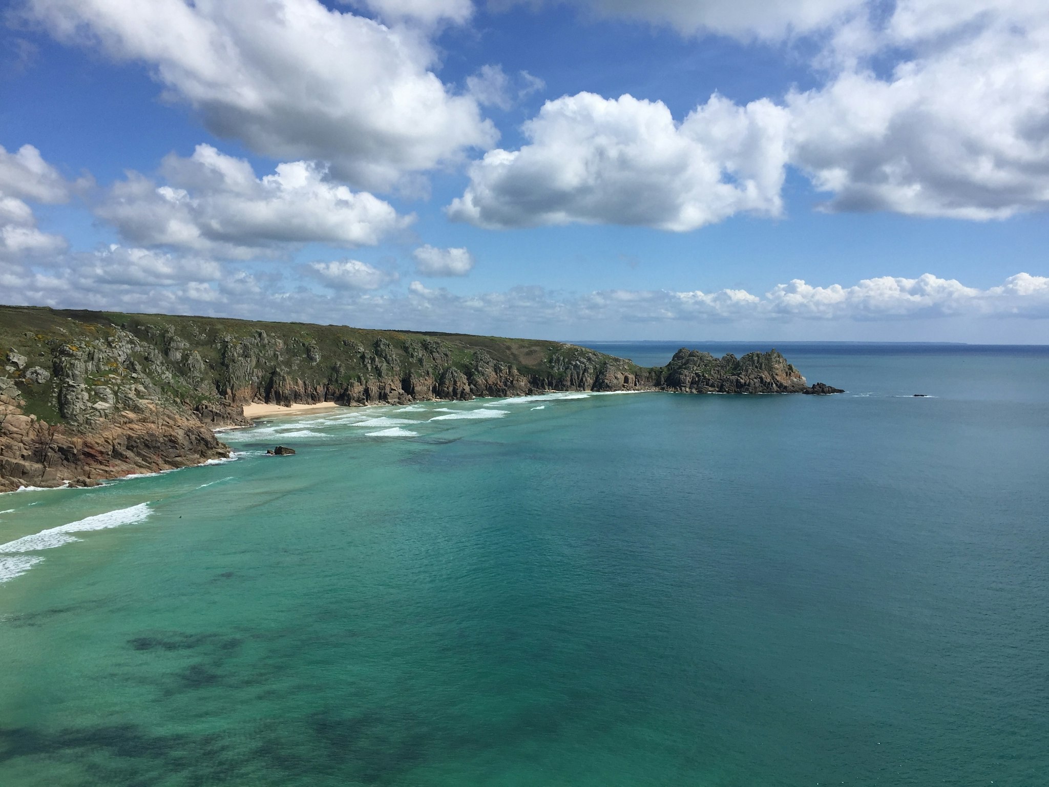 Aerial view of a scenic coastline, featuring cliffs, rocky shores, and the vast ocean meeting the sky.