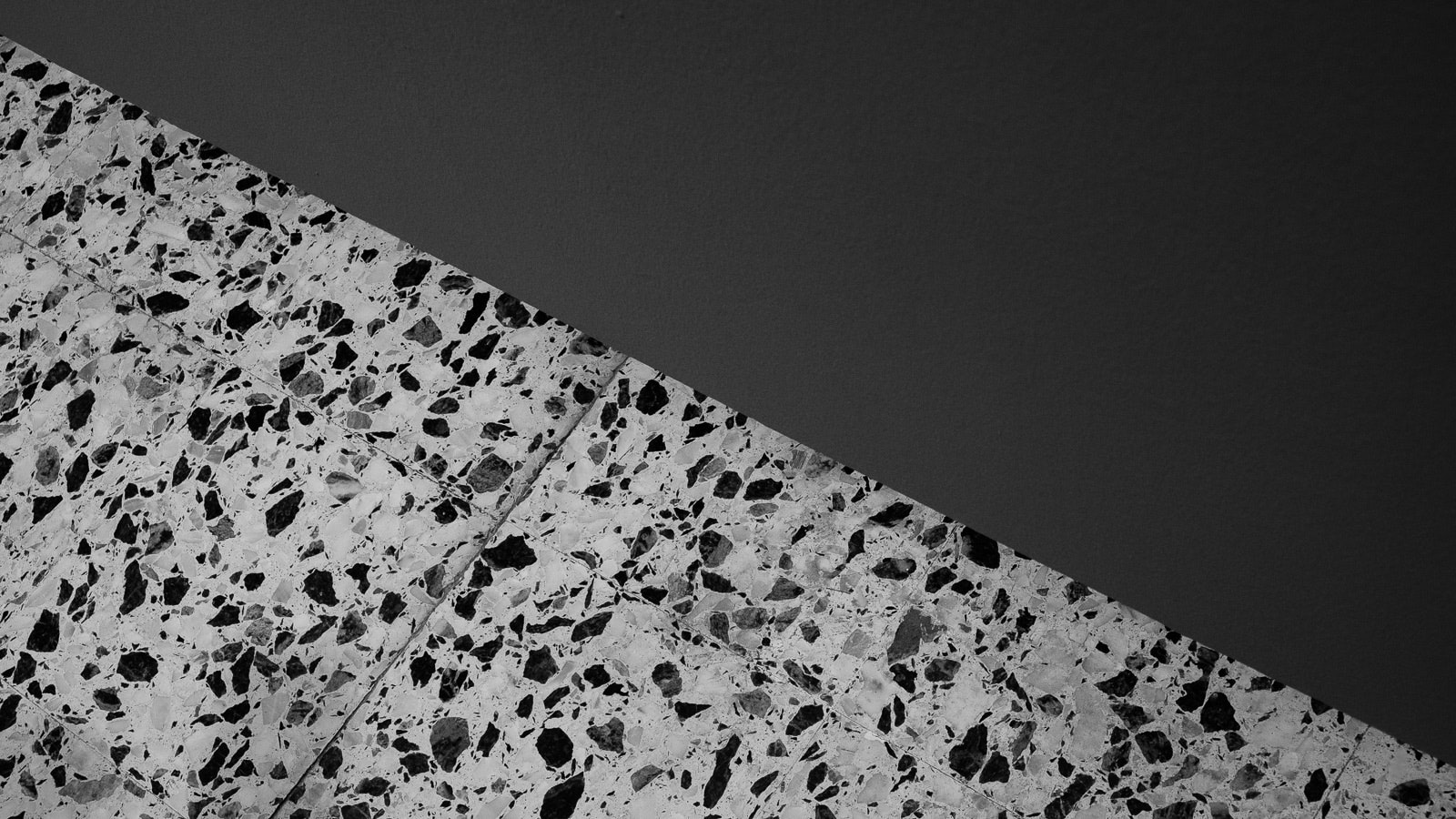 Pavimento in terrazzo grigio, con scaglie di marmo grigie e nere, accostato a una parete dipinta di grigio scuro.