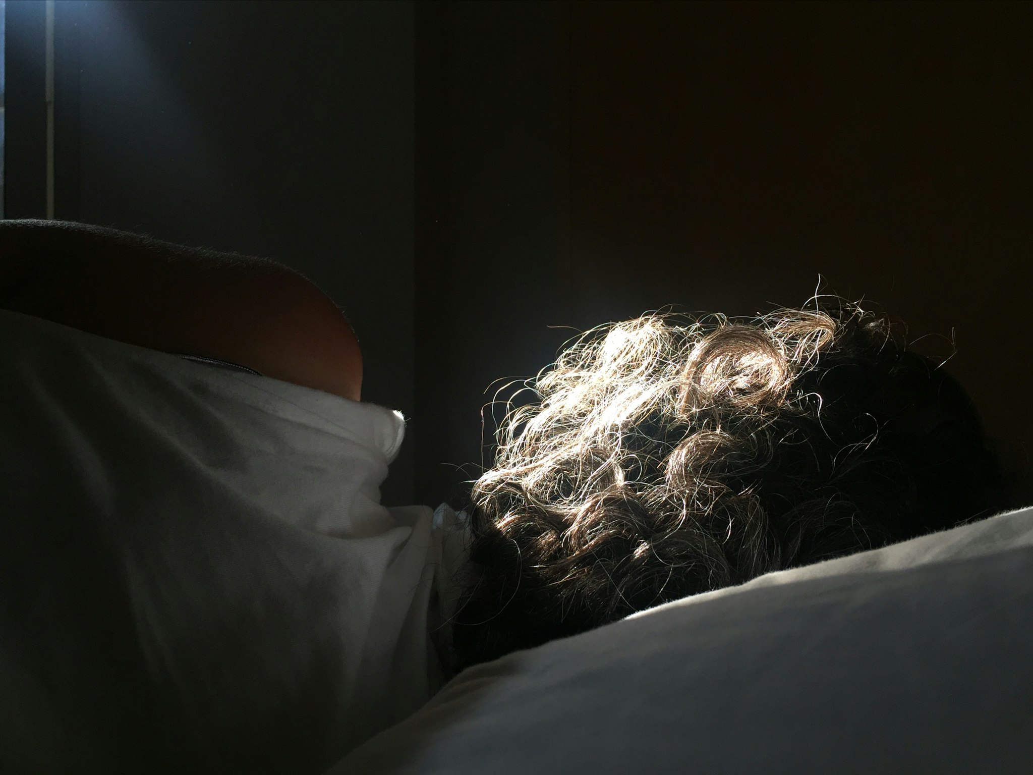 A person lying in bed with the sunlight shining on them. The image is grainy and blurred.