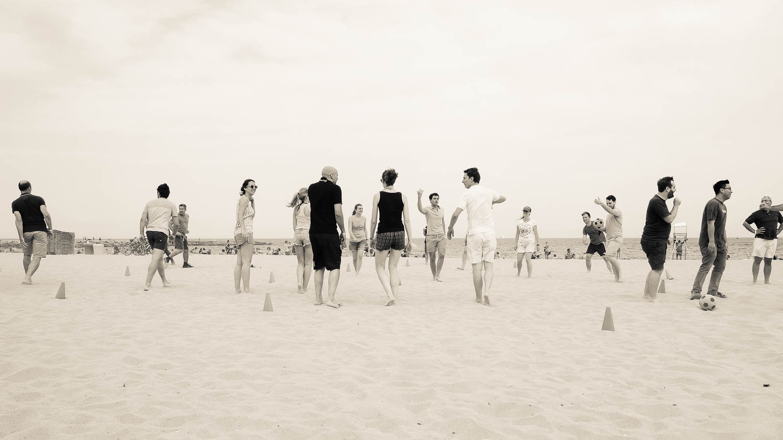 Una squadra di persone gioca pallavolo sulla spiaggia con uno sportello all'aperto e il cielo nublato. I giocatori sono posizionati strategiciamente attorno al tralcio.