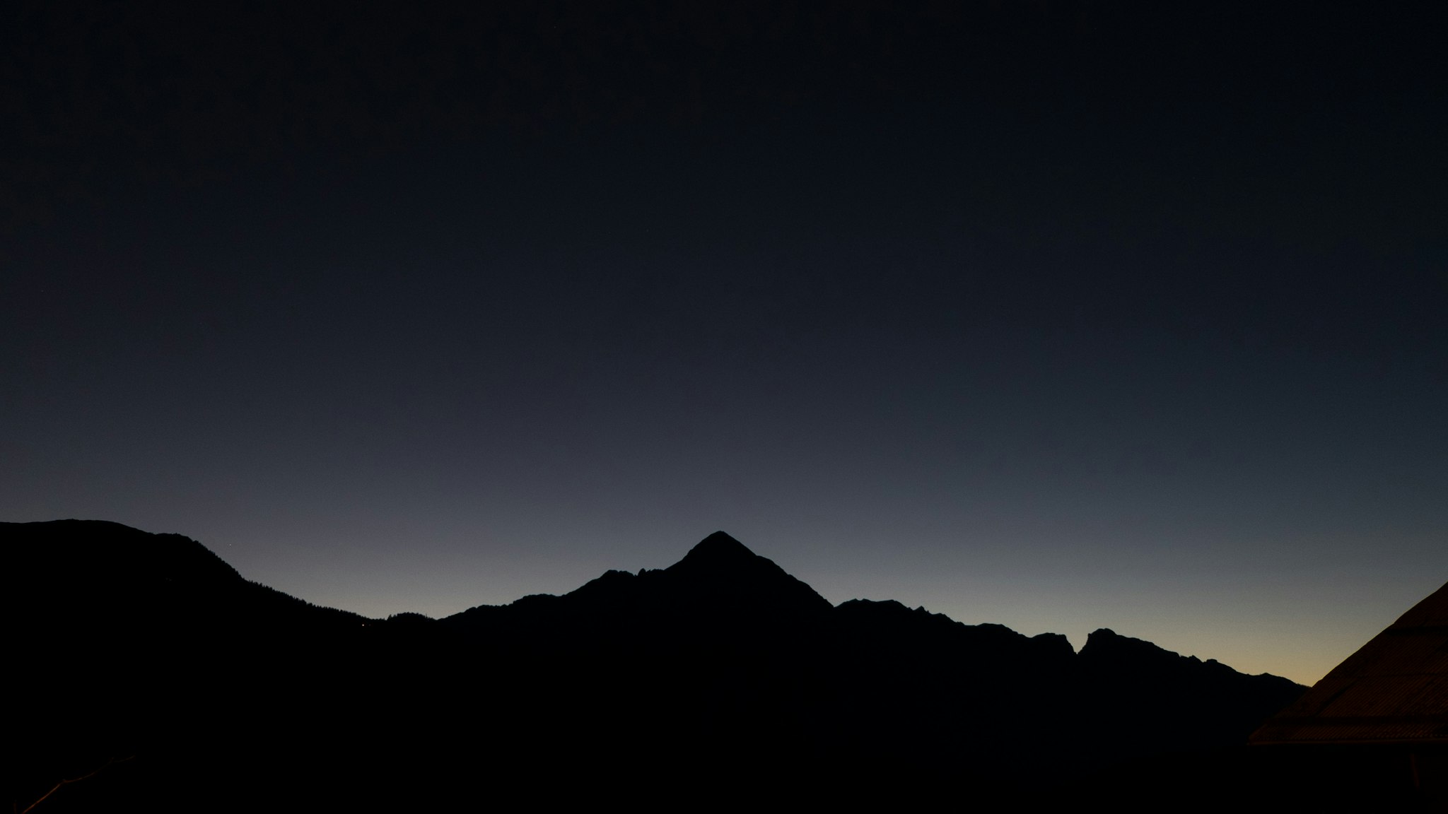 Scena notturna di montagne con linea del cielo, che mostra il contorno della punta in silouetta contro sfondo stellato. Una foto panoramica verticale rileva la vasta dimensione dello scenario.