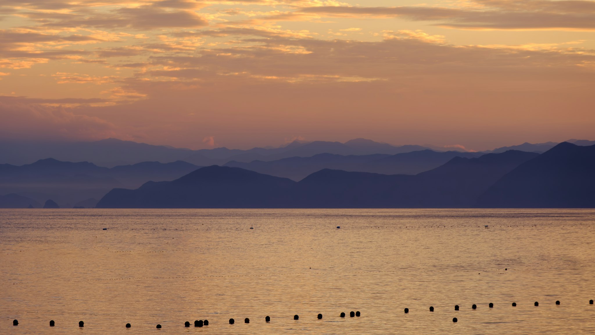A picturesque view of a serene lake at sunset, with silhouettes of trees and the horizon.