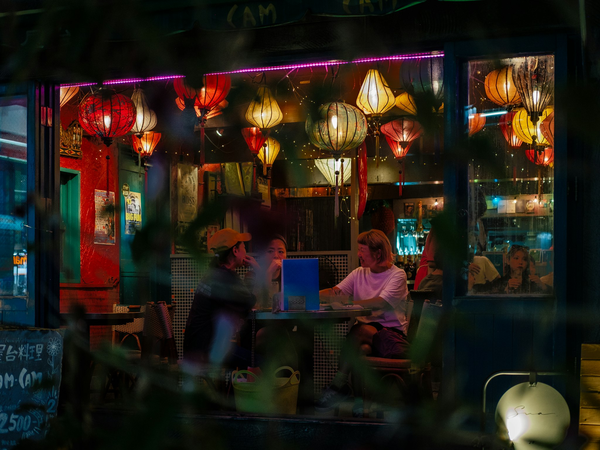 A vibrant night scene with neon lights, lanterns, and people at an outdoor cafe.