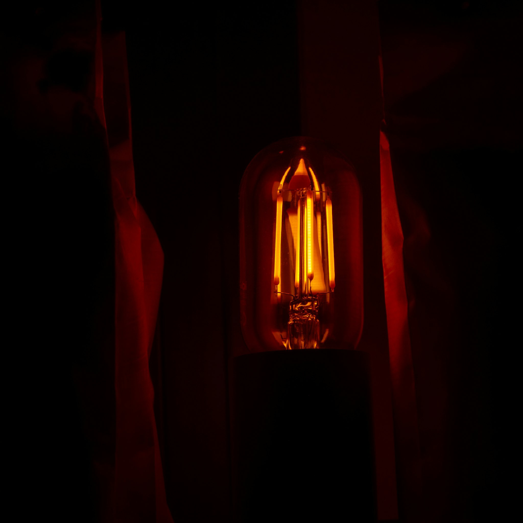 Una lampada incandescente con un filetto visibile. La luce è accesa, emanando una luce calda. La luce sembra essere di forma tradizionale di una lampada incandescente, potenzialmente indicando un modello o stile più vecchio.