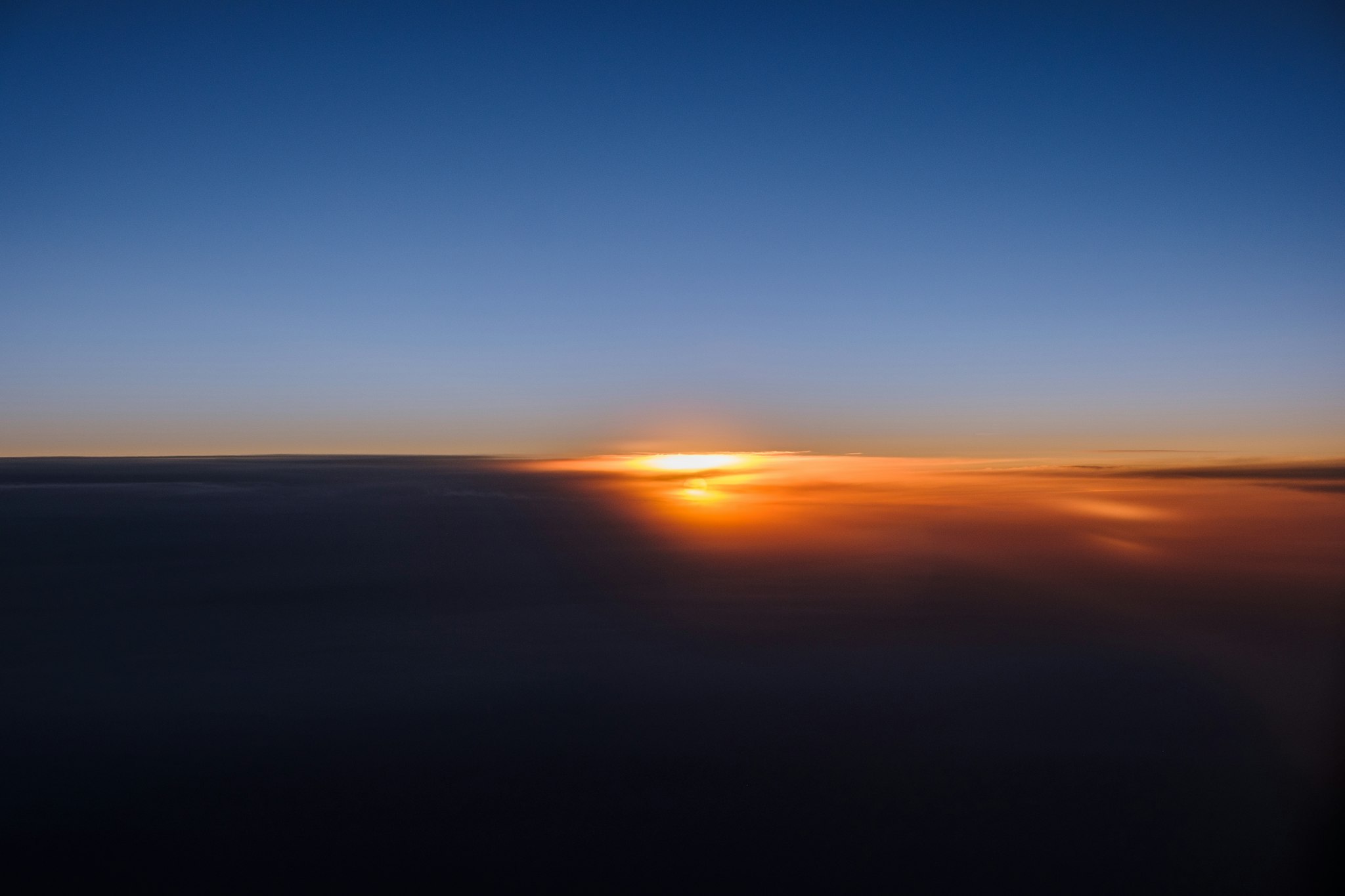 A stunning aerial view captures the horizon at sunset, with a vibrant orange sun dipping below dark clouds and a deep blue sky above, exemplifying the beauty of nature.