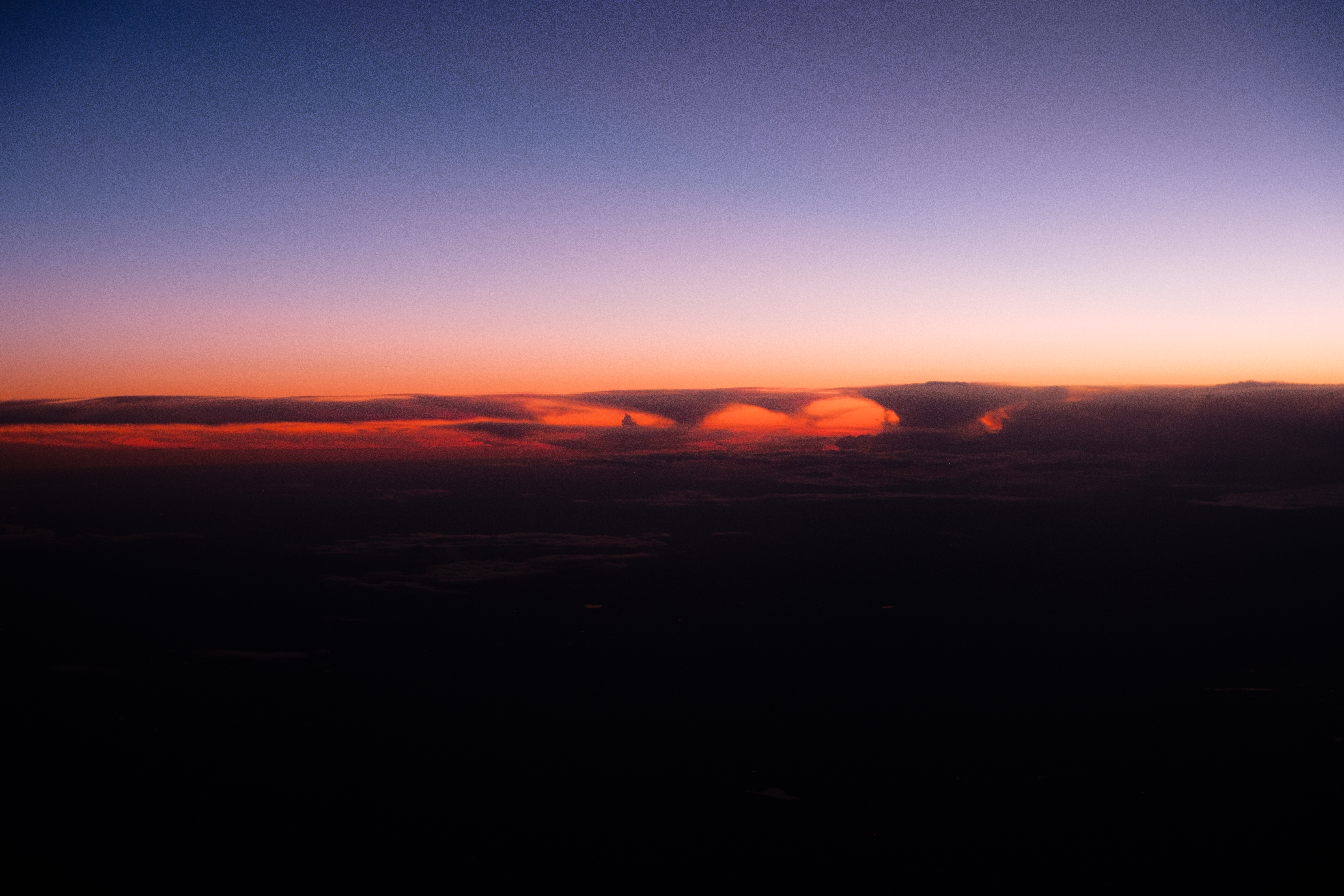 Tramonto spettacolare con nuvole arancioni sopra un paesaggio scuro, mentre il cielo sfuma dal blu al viola.