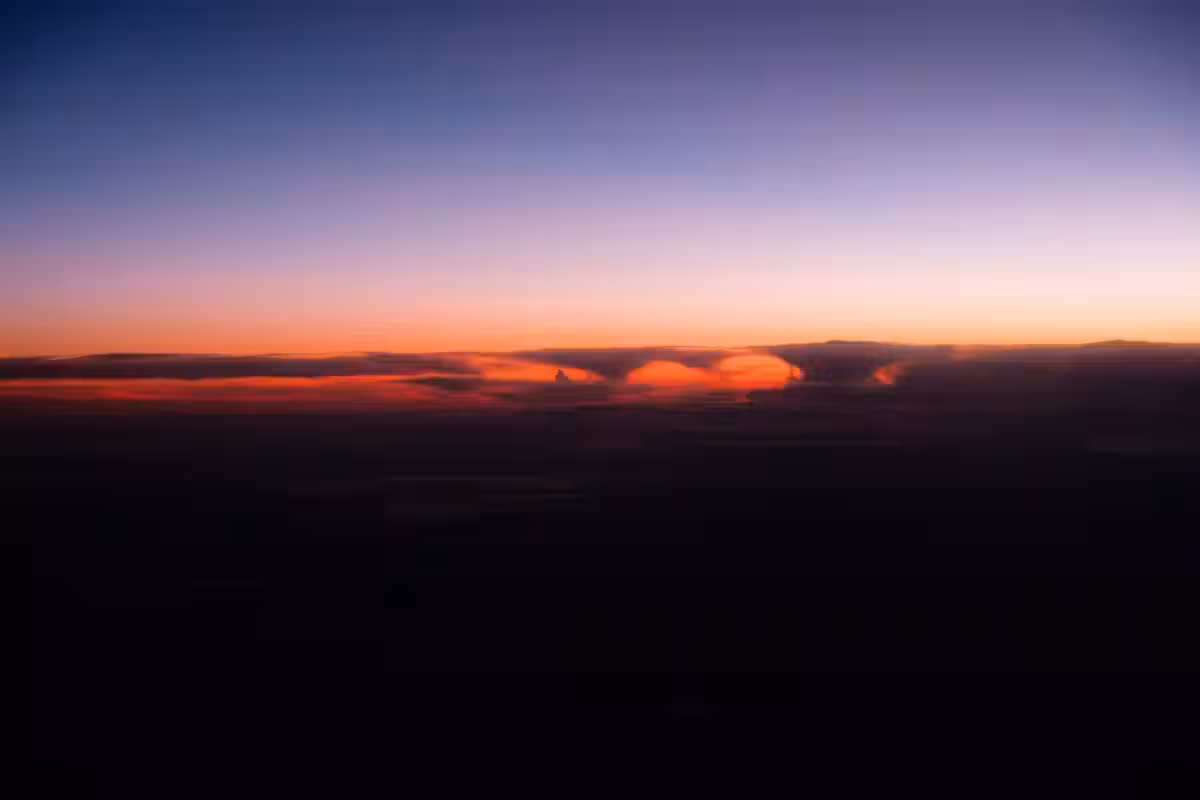 Tramonto spettacolare con nuvole arancioni sopra un paesaggio scuro, mentre il cielo sfuma dal blu al viola.