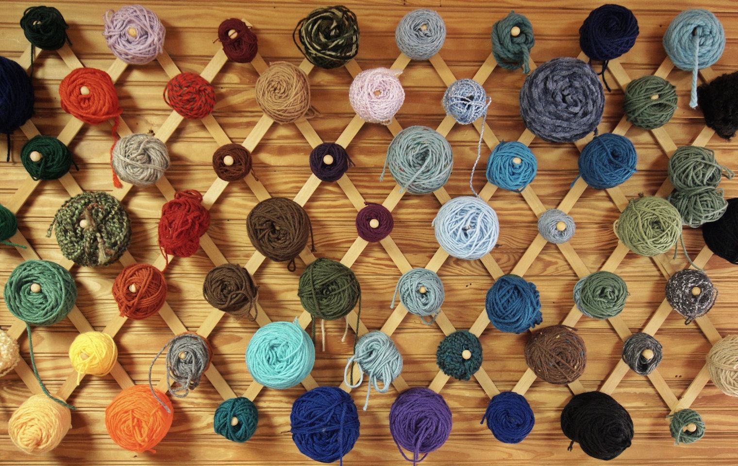 A collection of yarn cakes, all different colors and different sizes, hanging on a wall.