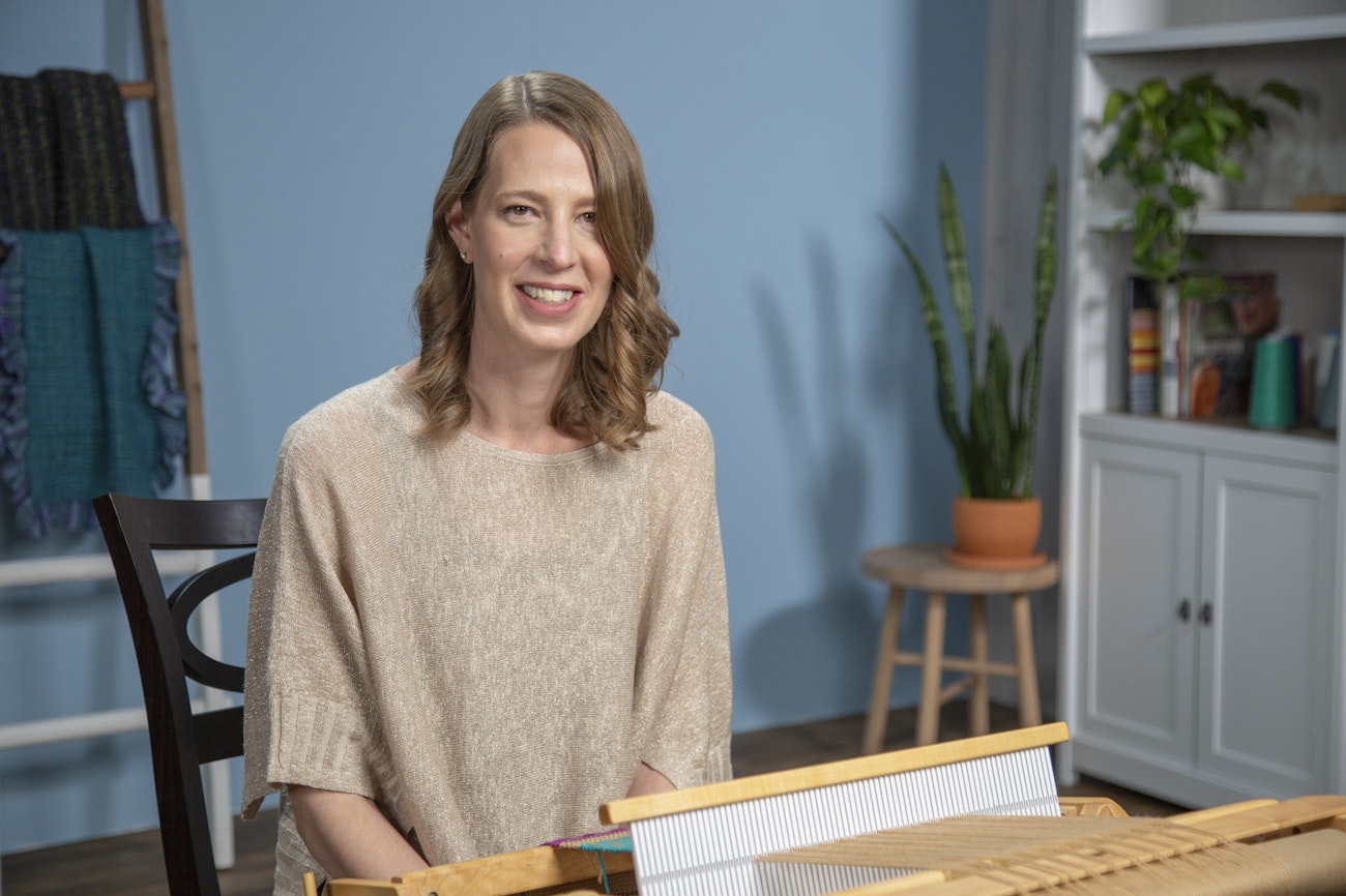 Sara Goldenberg White in sitting in front of a loom, smiling.