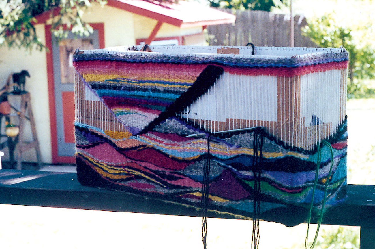Cardboard box covered in warp with tapestry weaving in progress