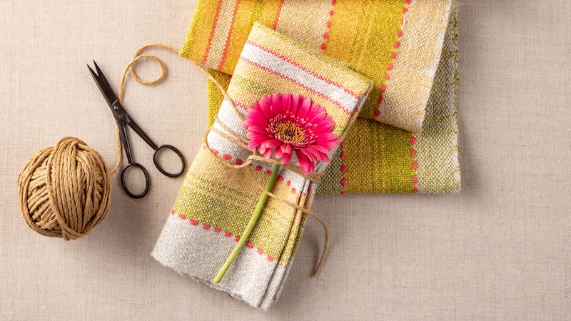 Woven napkins with a ball of yarn, scissors, and flower.