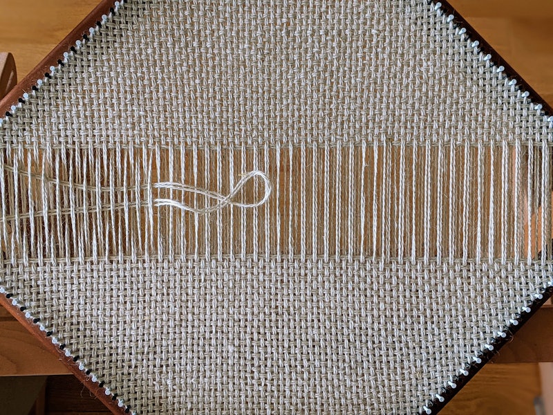 A square pin loom with a partially woven square using the continuous-strand method