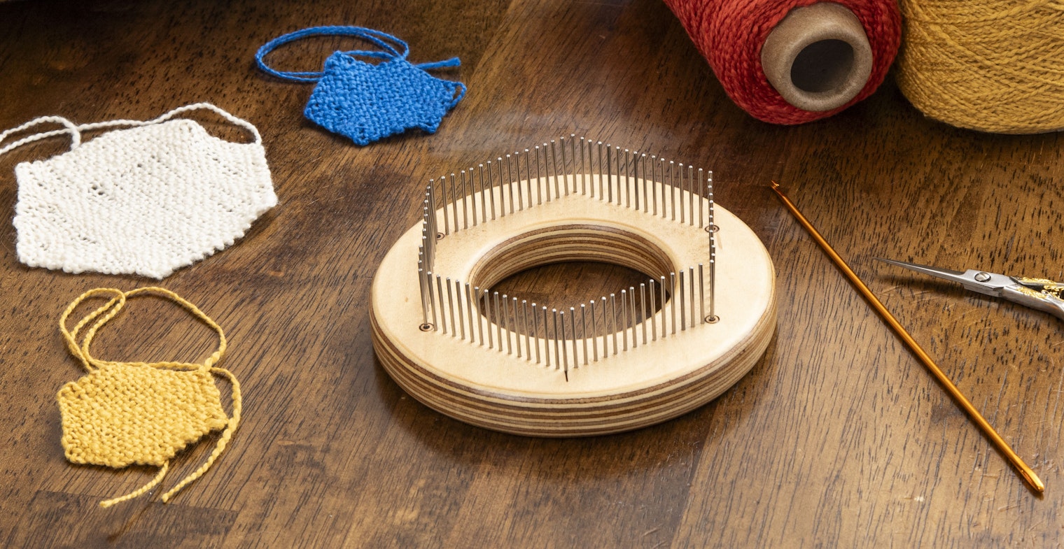 On a wood table from left: Three hexagon pin loom pieces, a hexagon pin loom, yarn, weaving needle and scissors.