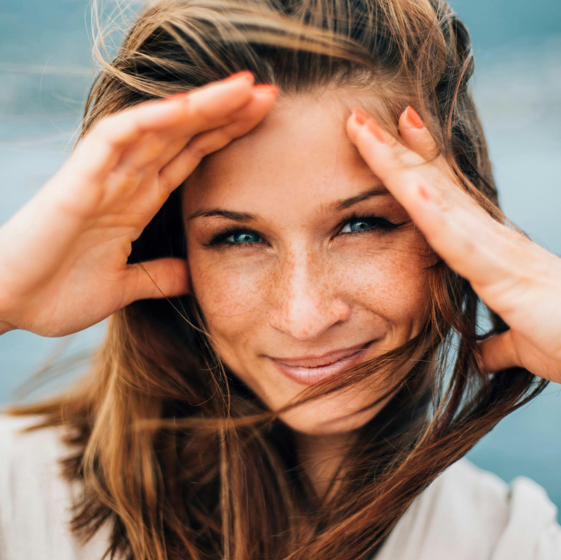 woman with brown hair blowing in the wind and her hands to her head