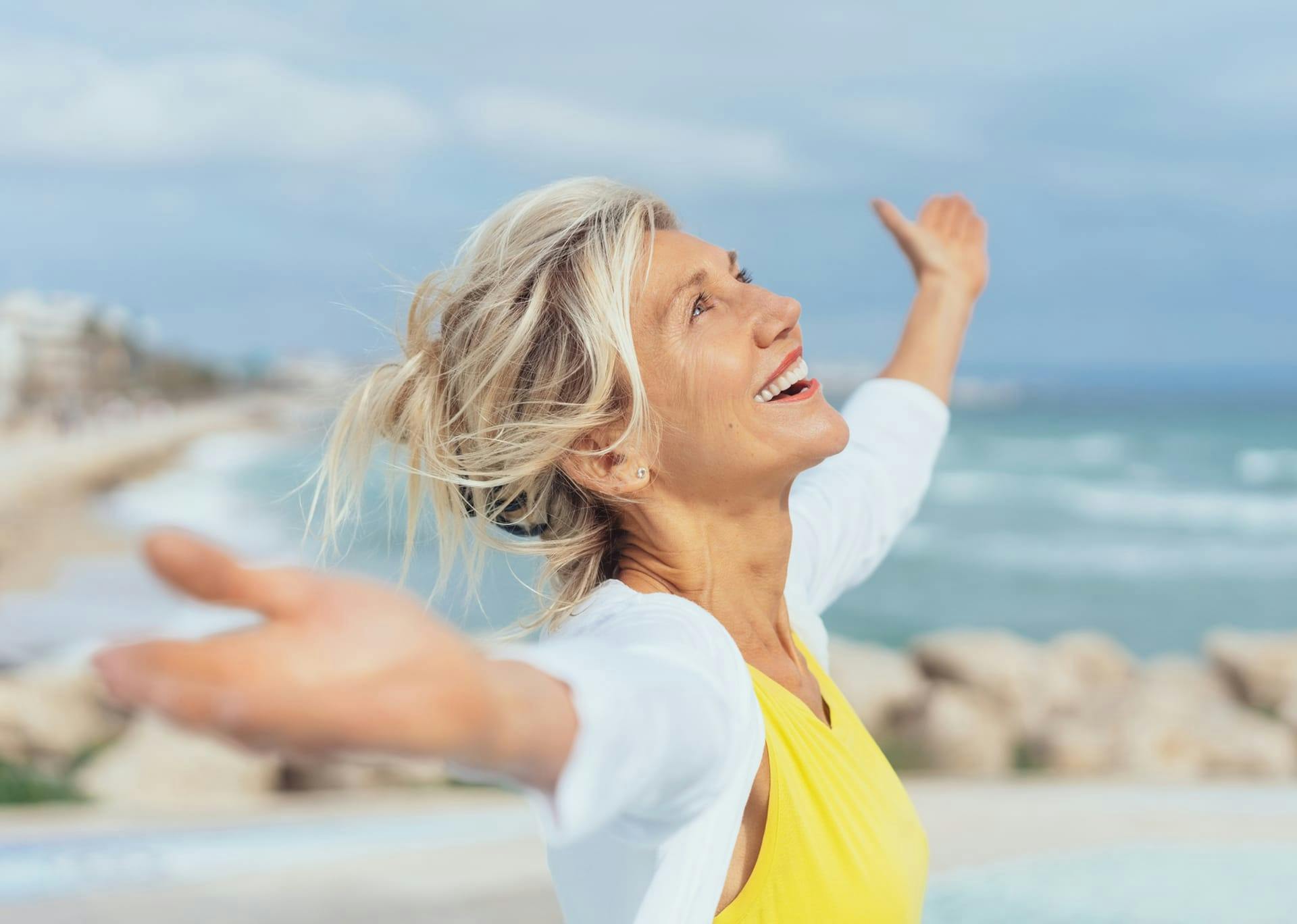 woman smiling with her arms out on the beach