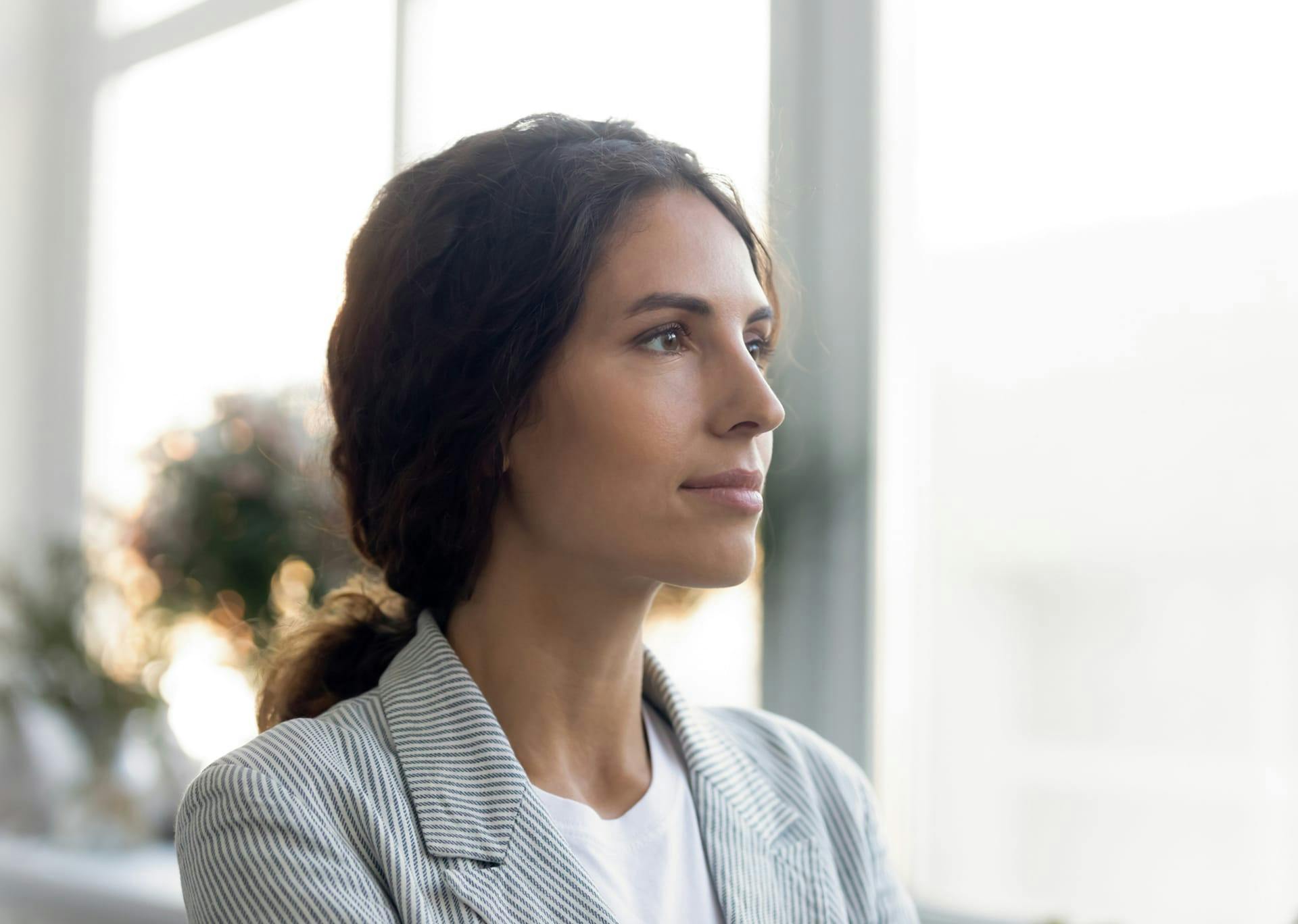 woman with brown hair tied back and a window in the background