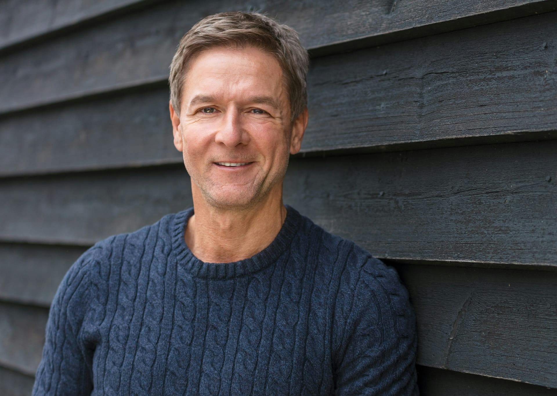 man smiling and standing against a wall
