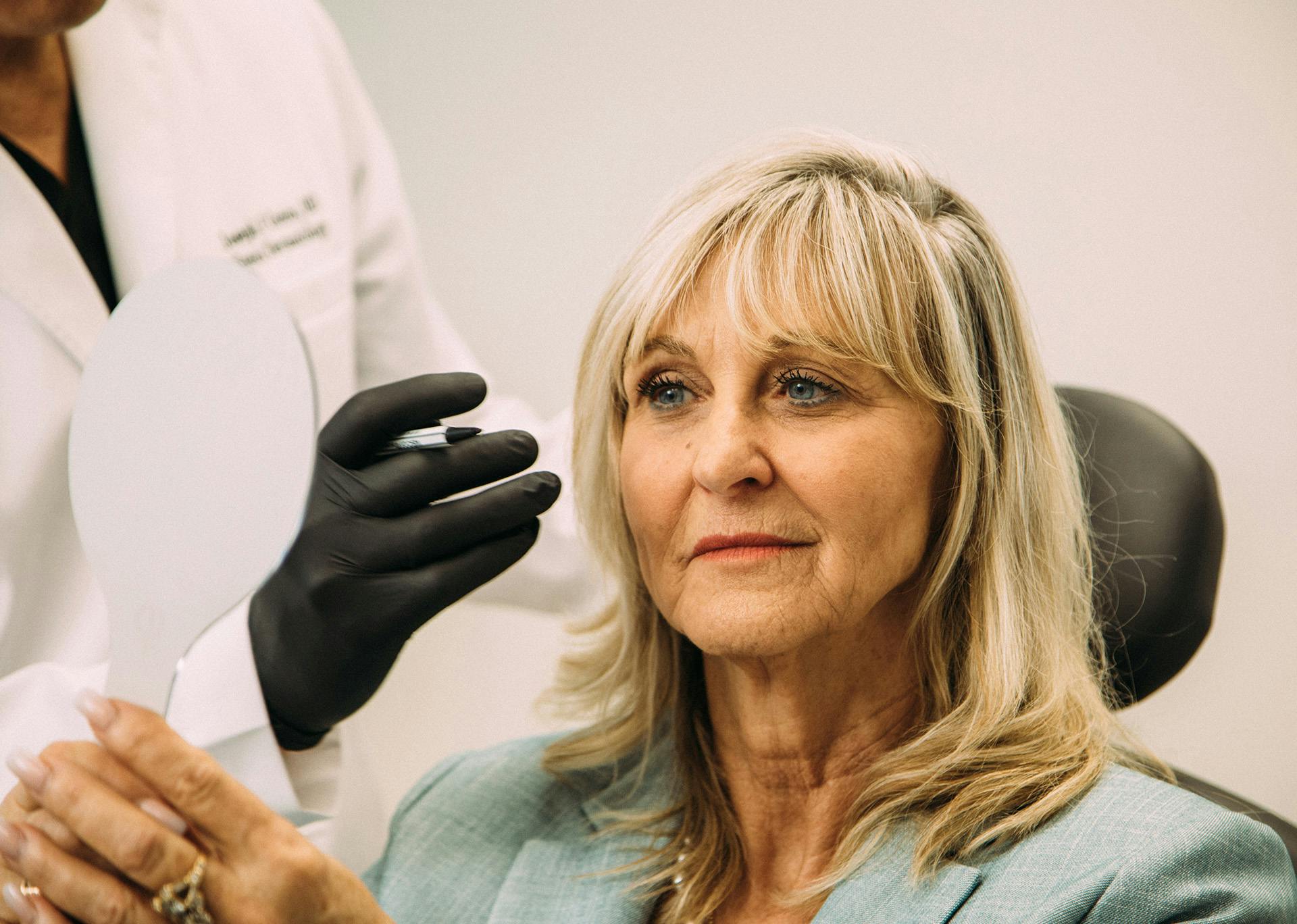 woman looking in the mirror and Dr. Greco standing next to her