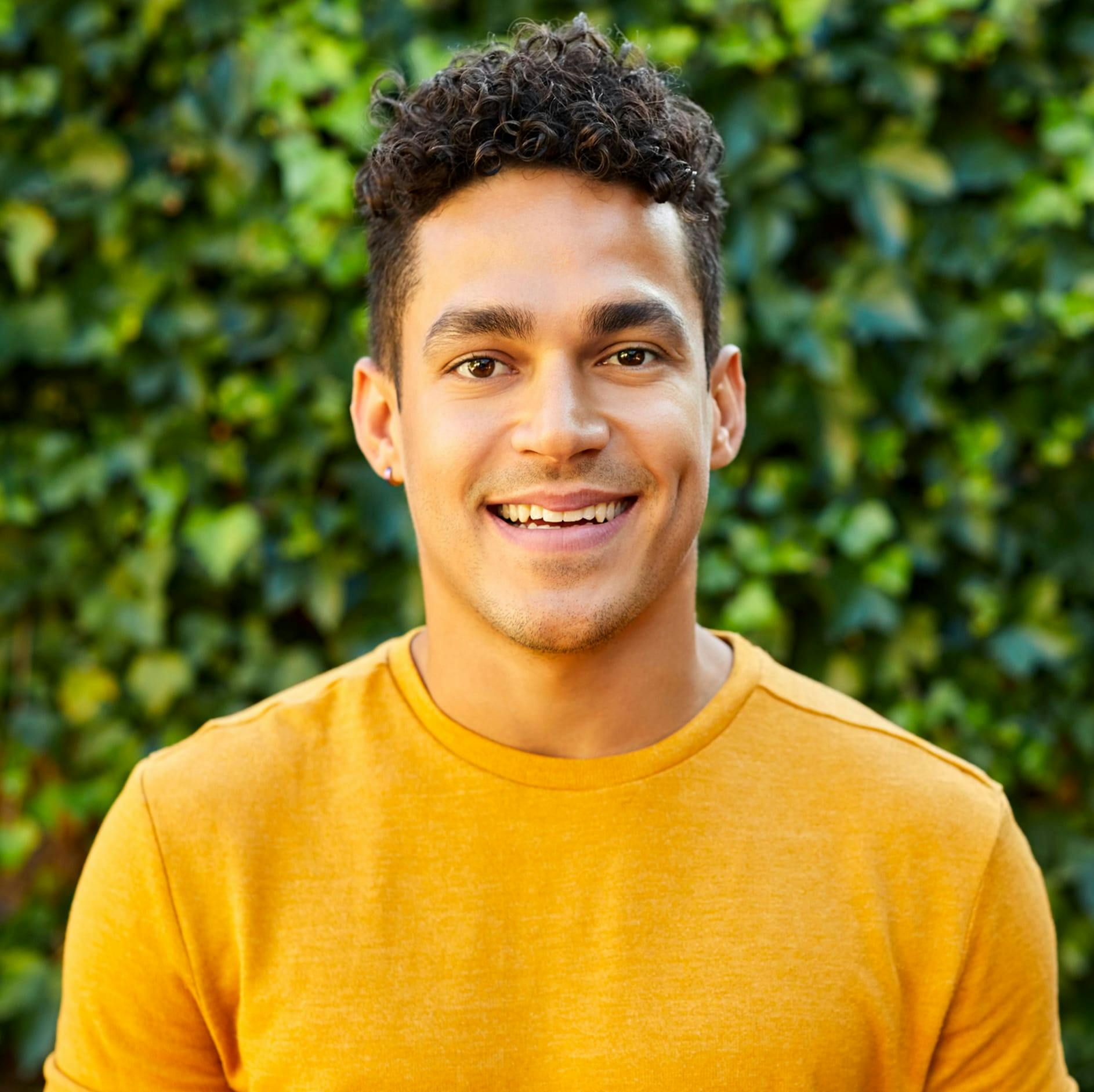 man in a yellow shirt smiling with green plants in the background
