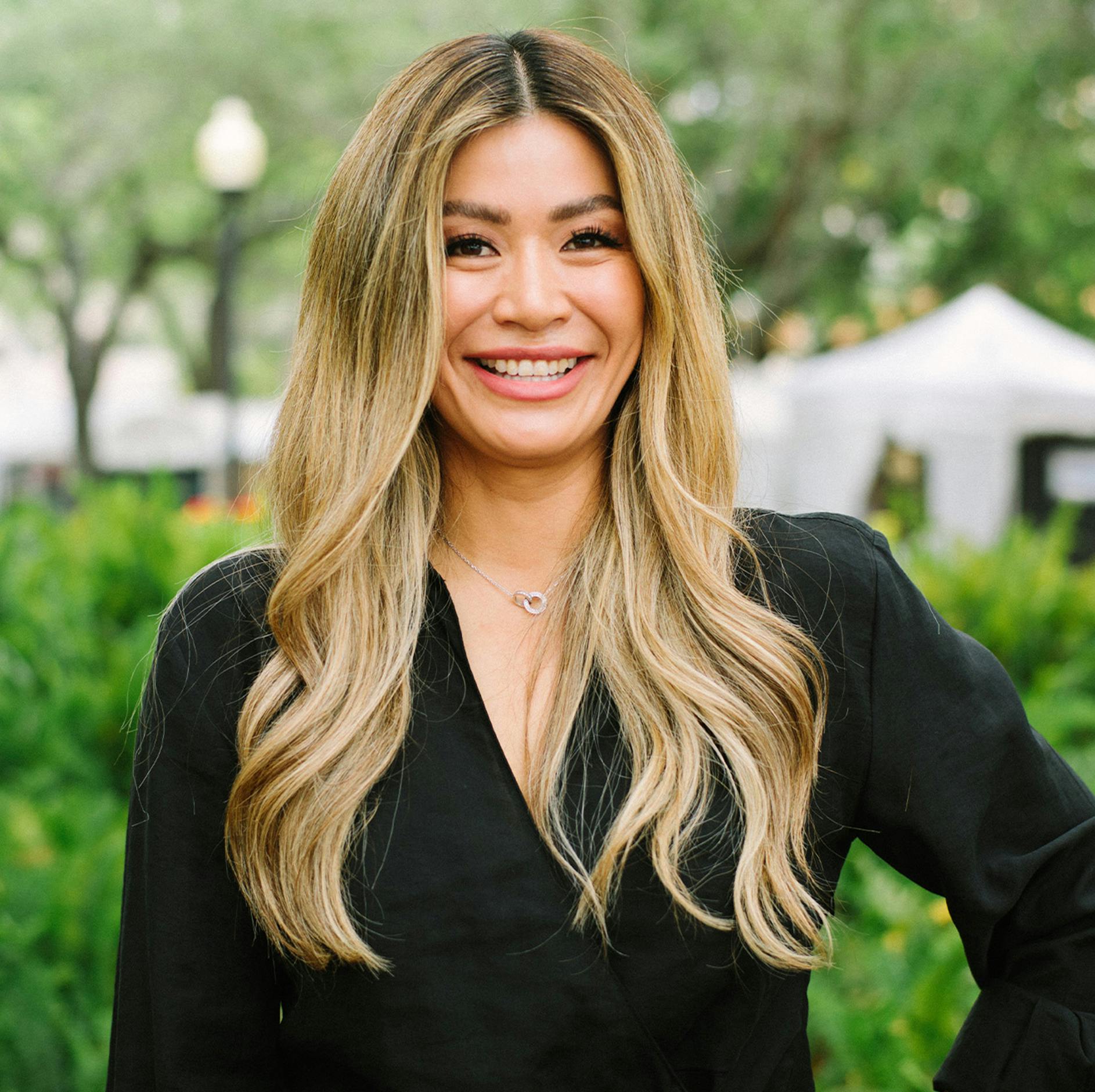 Vicky Greco smiling with a whiten tent and green plants in the background