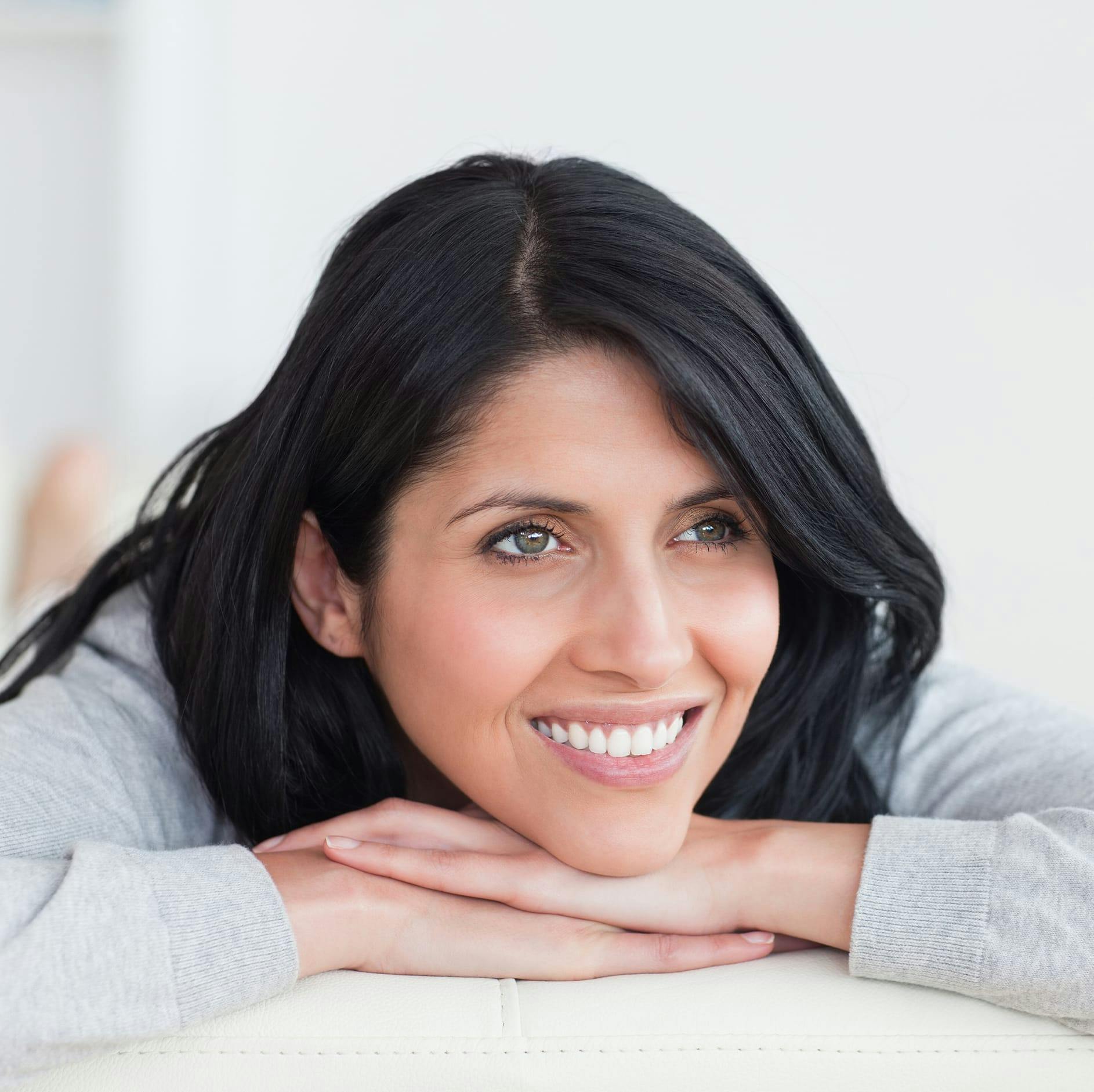 woman smiling with black hair and her head resting on her hands