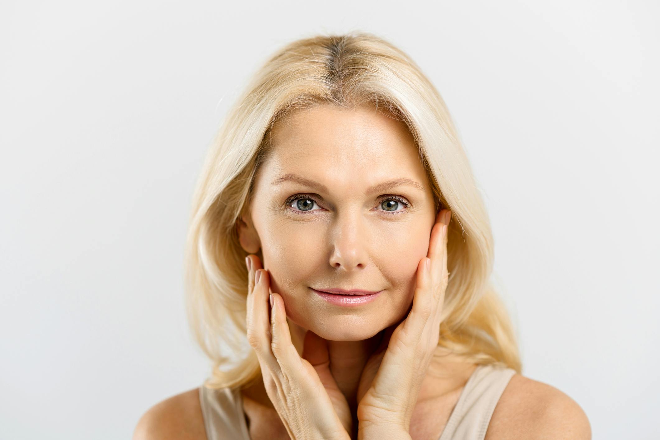 woman with blonde hair and touching her face and smiling