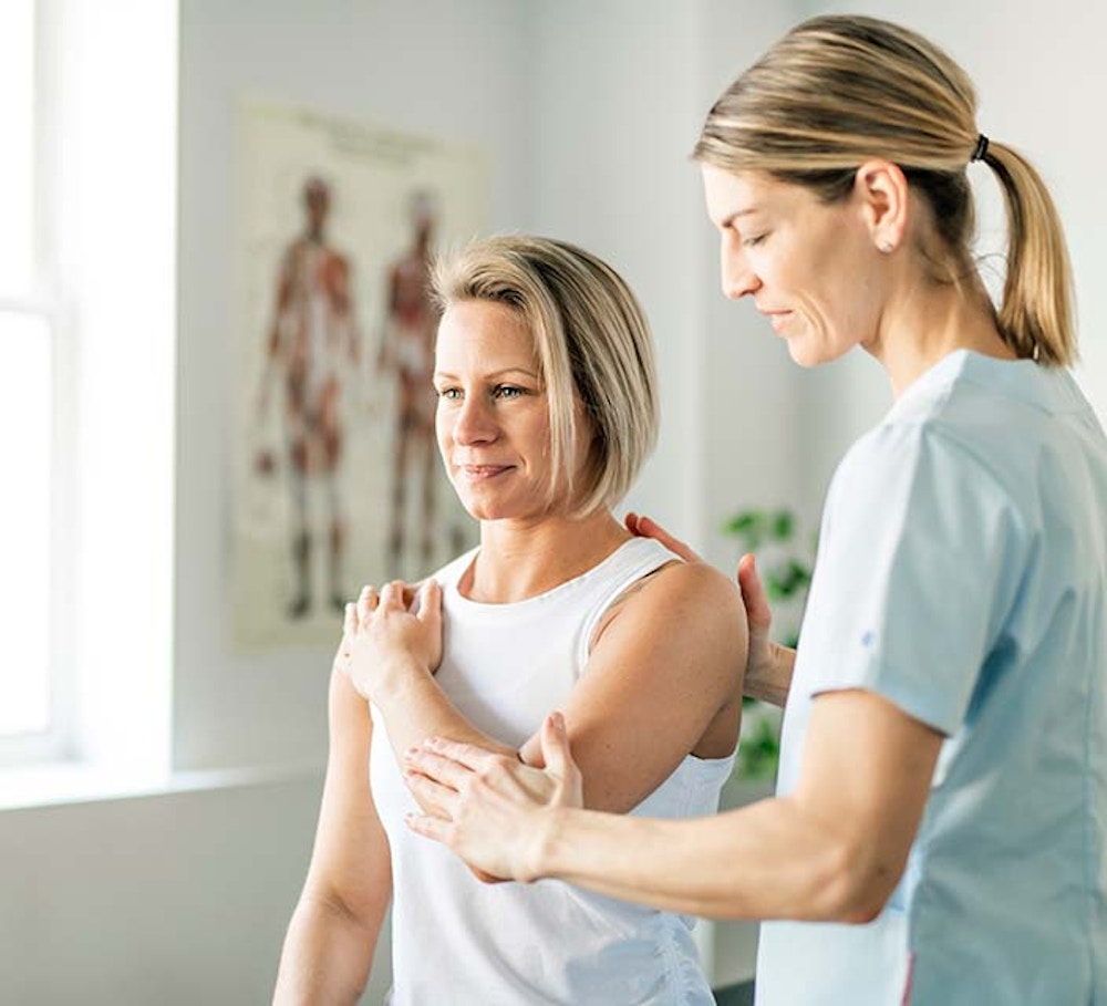Female Physiotherapy Assistant assisting female patient with shoulder mobility