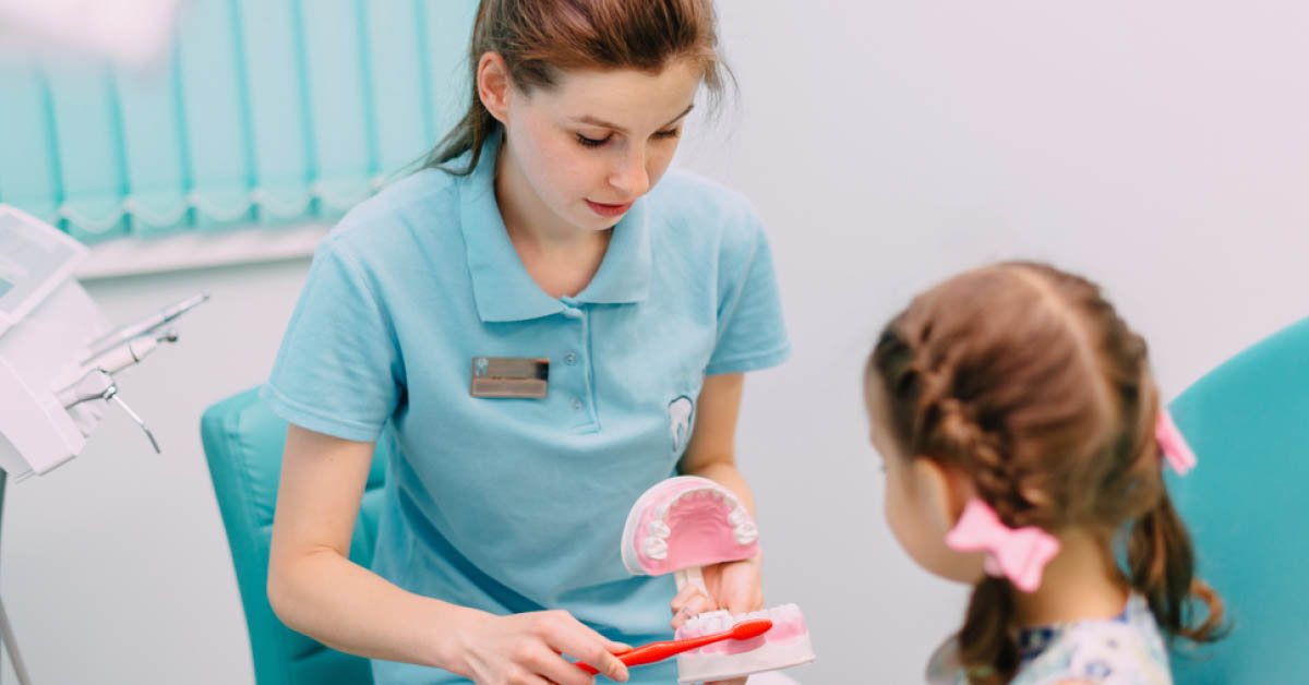 Dental assistant showing child how to brush teeth