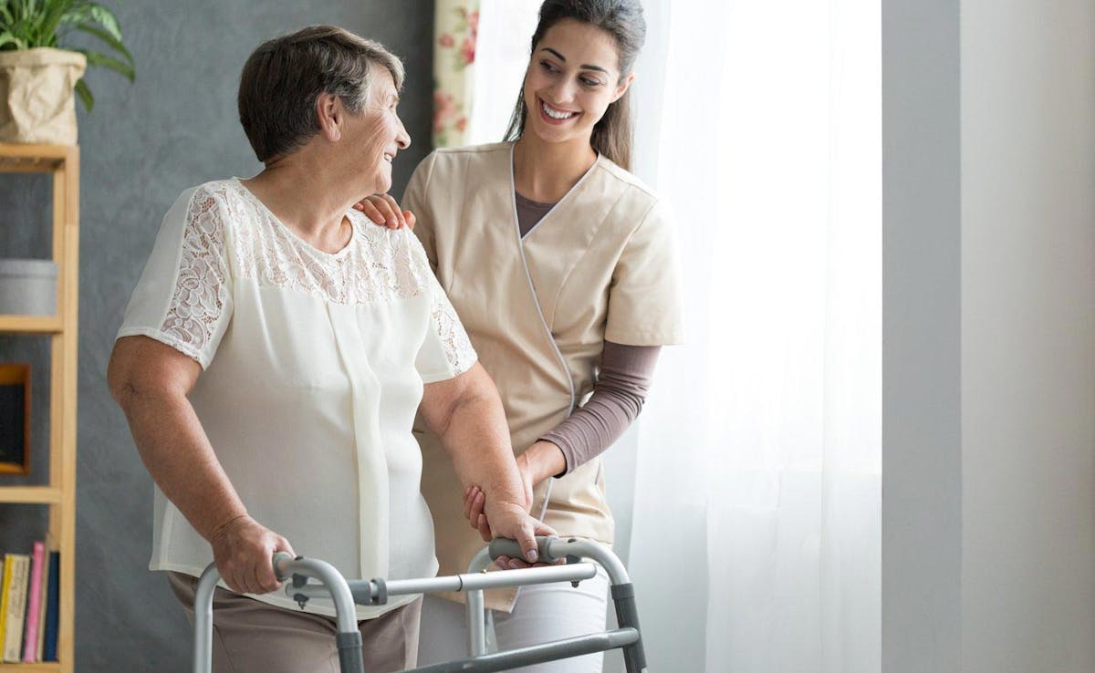 Healthcare professional helping elderly female with her walker