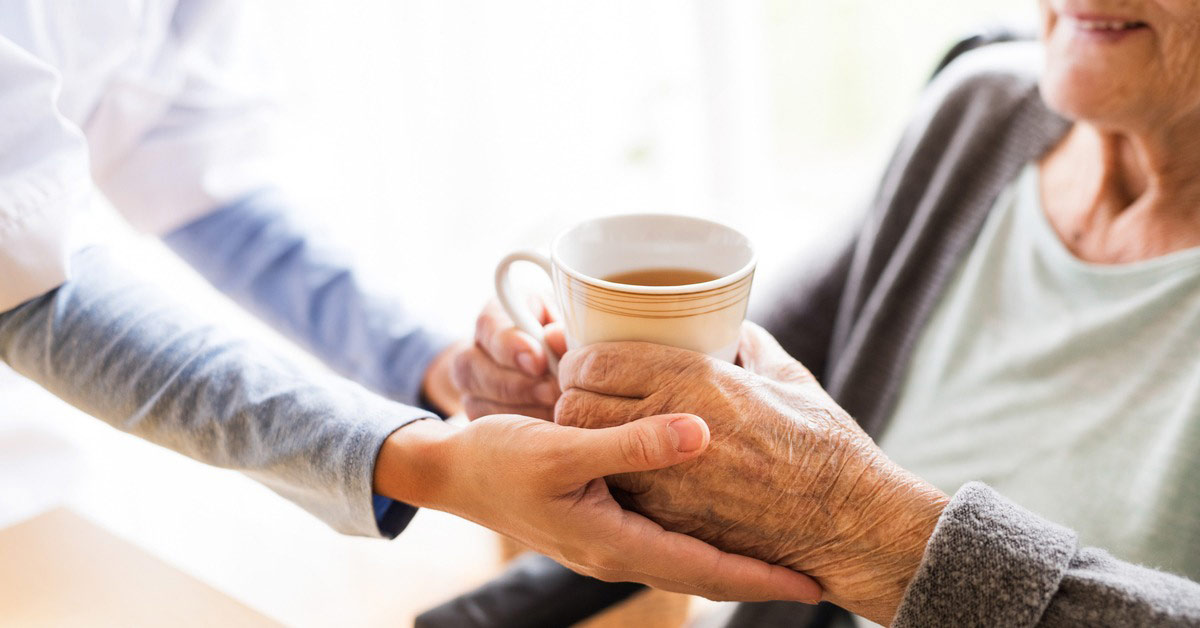 Career giving a hot drink to an elderly person