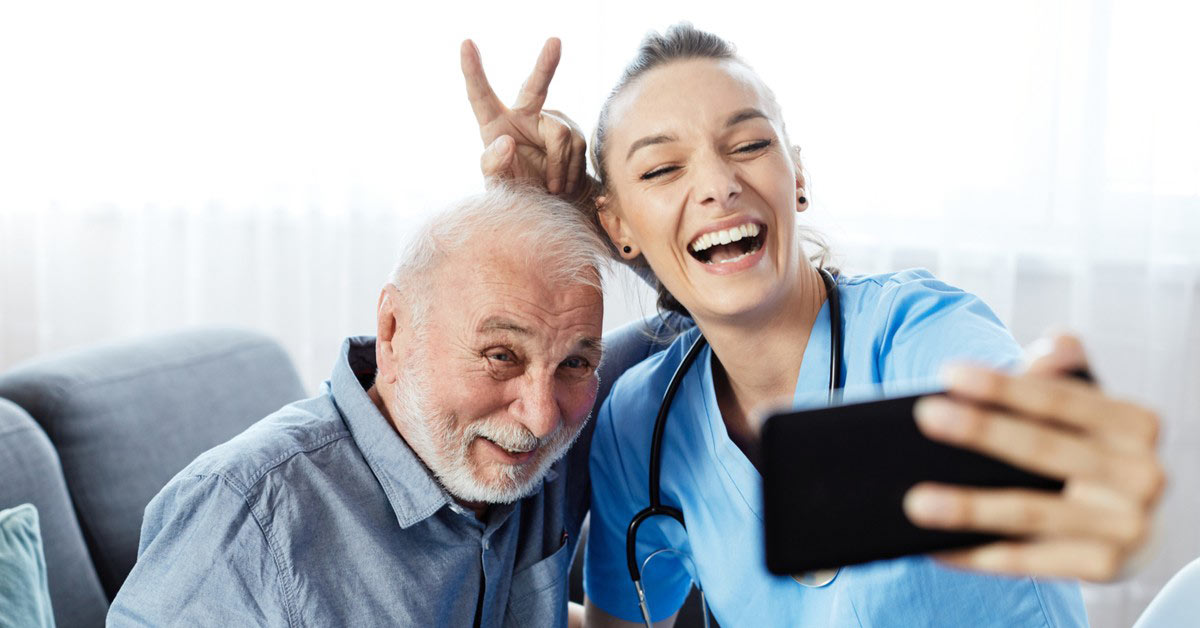 An elderly man and his nurse take a photograph together