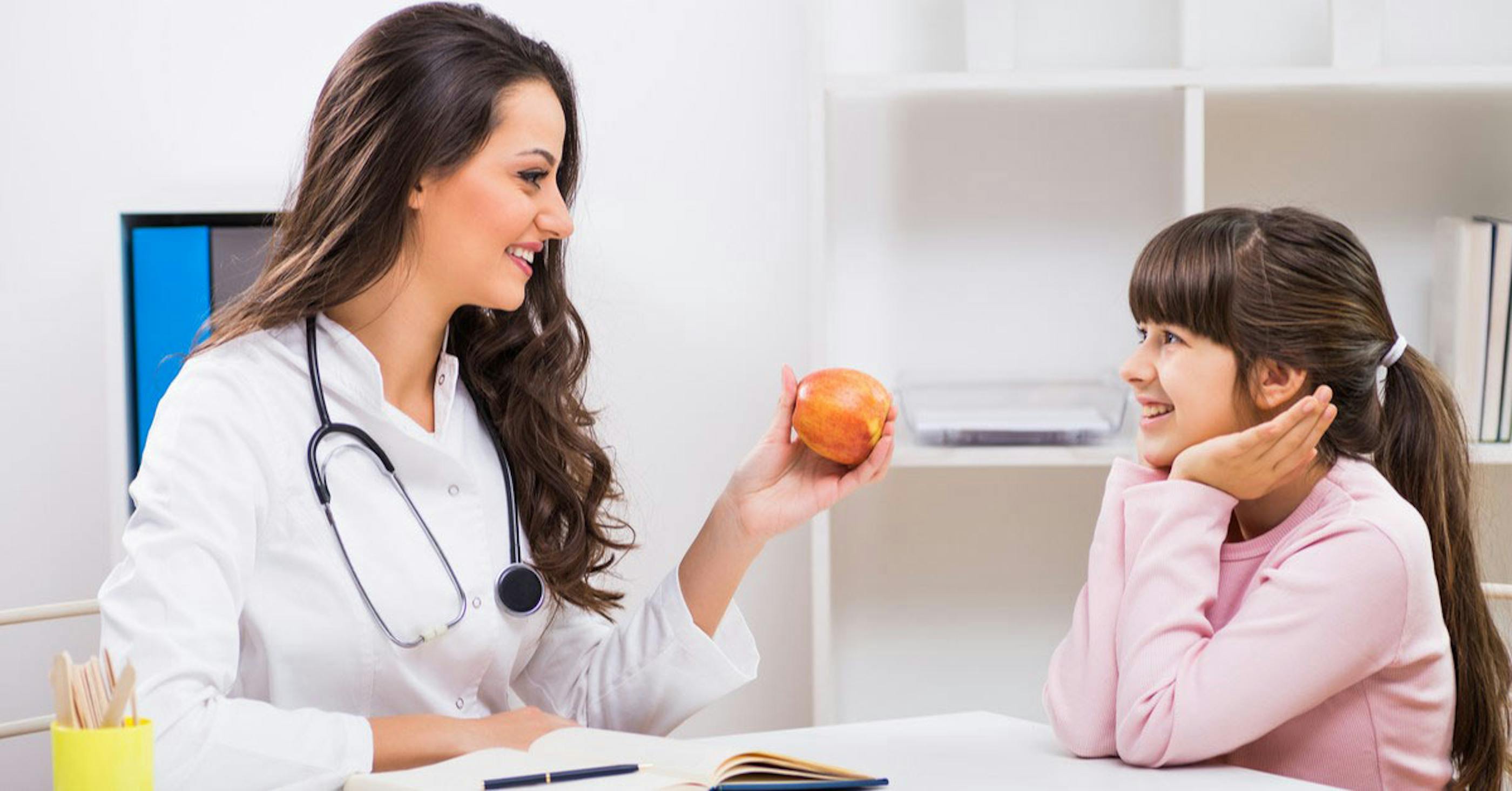 Nutritionist talking to young girl with apple in hand