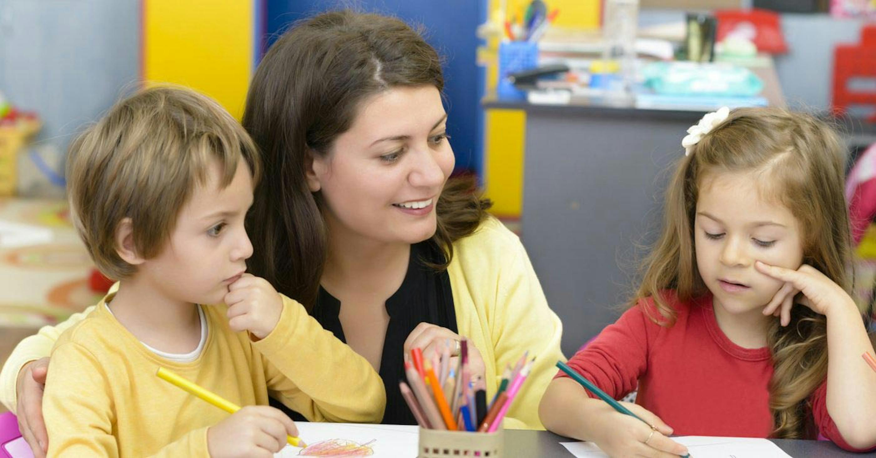 Childcare worker helping two young students with their drawings