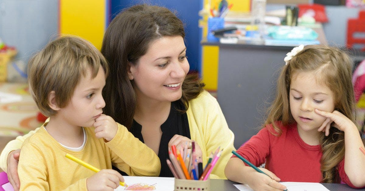 Childcare worker helping two young students with their drawings