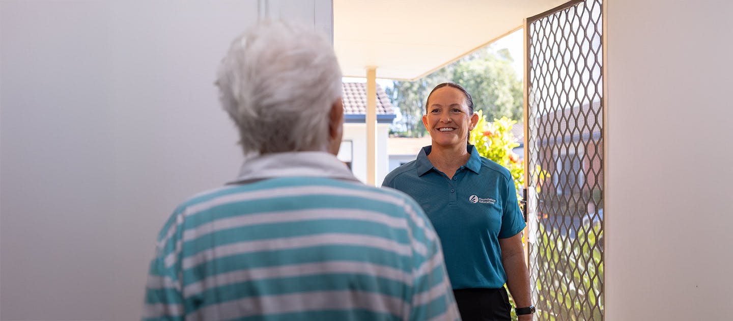 Foundation Education individual support worker smiling and greeting an elderly client at the front door of a residential home.