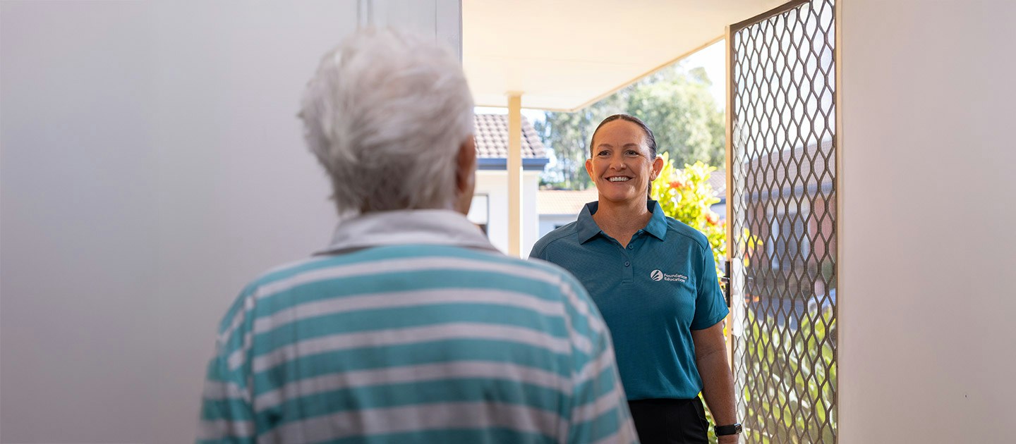 Foundation Education individual support worker smiling and greeting an elderly client at the front door of a residential home.
