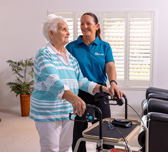 Foundation Education support worker assisting an elderly woman using a mobility walker inside a home.