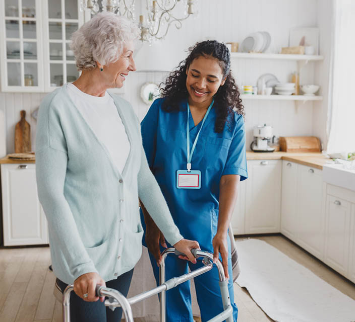 Individual support worker assisting an older woman using a mobility walker in her home