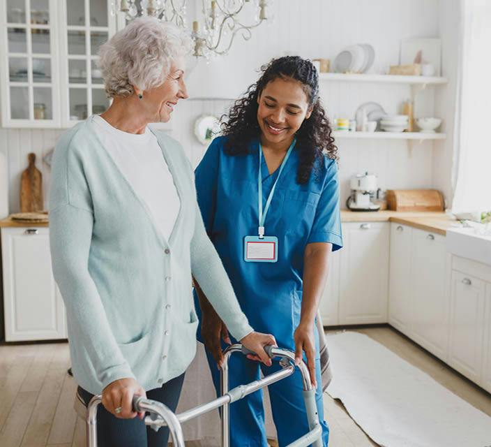 Individual support worker assisting an older woman using a mobility walker in her home