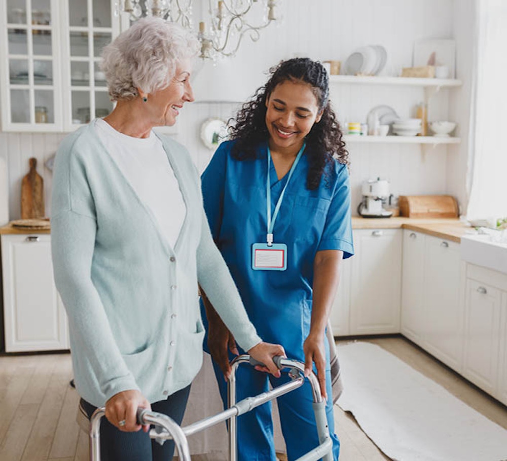 Individual support worker assisting an older woman using a mobility walker in her home