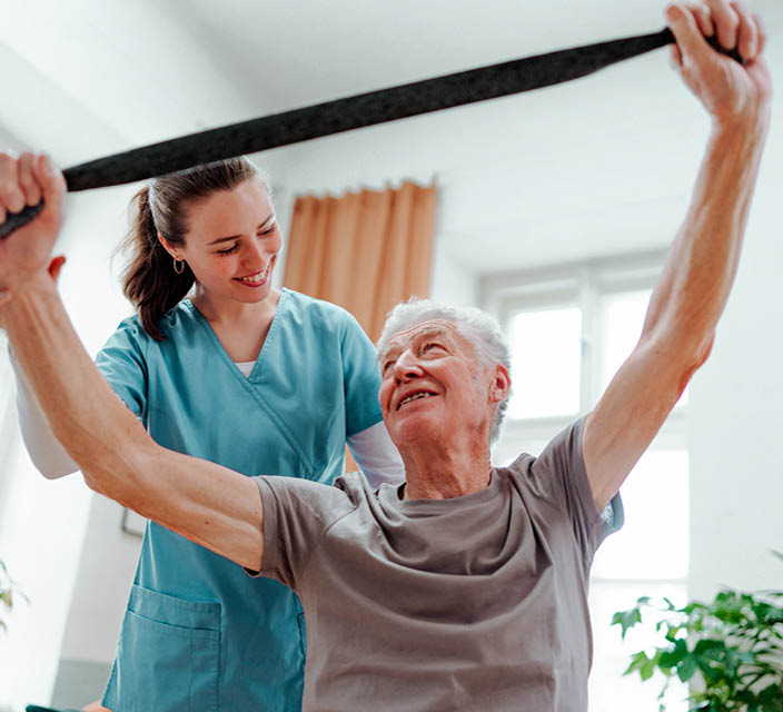Individual support worker assisting an older man with a resistance band exercise at home
