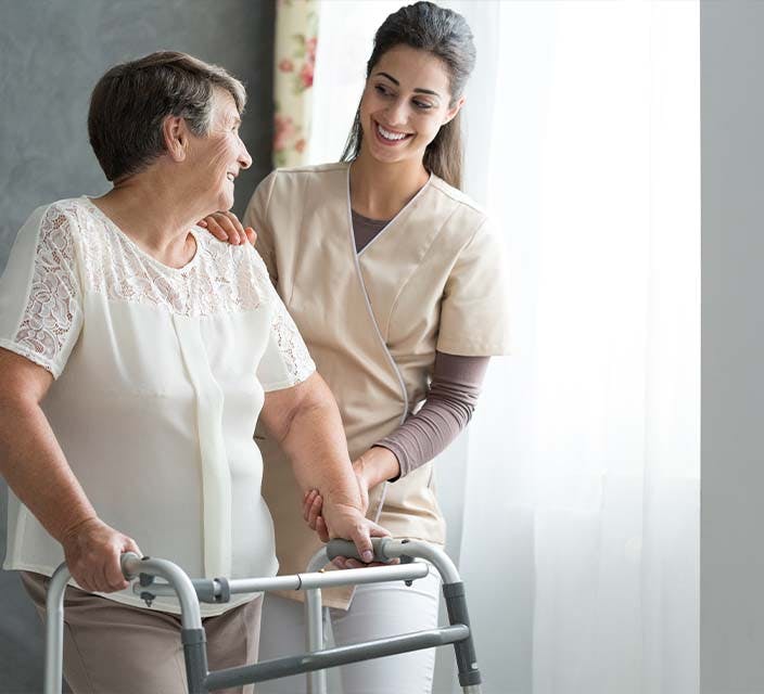 Health services assistant supporting an older person using a walking frame