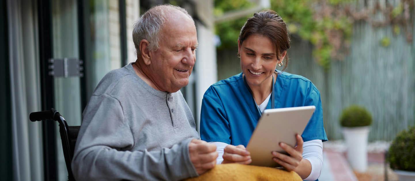 Disability support worker using a tablet with an older man who uses a wheelchair