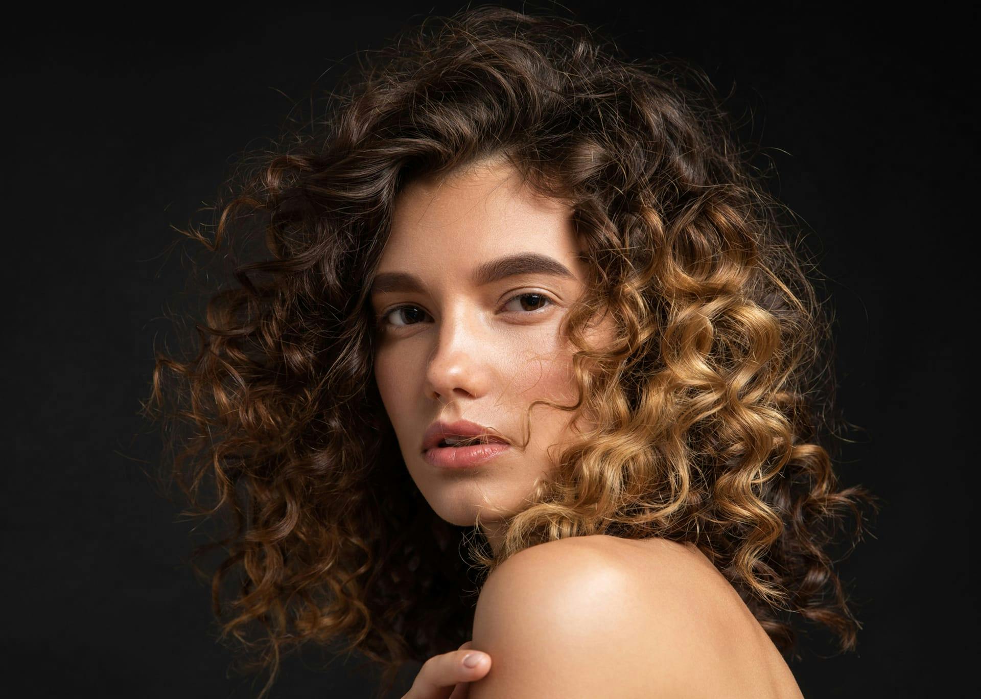 Beautiful woman with curly hair looking sideways at the camera.