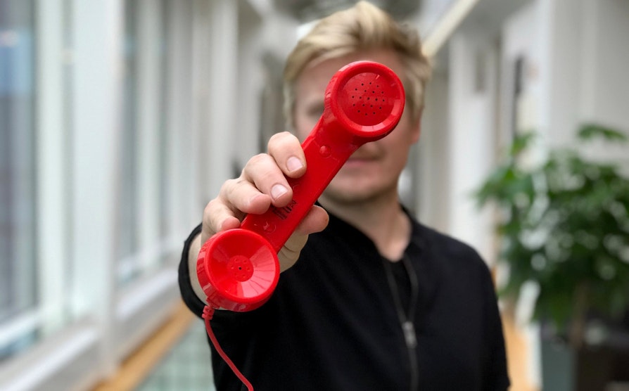 Norsk Tipping-ansatt holder frem et rødt telefonrør foran ansiktet.