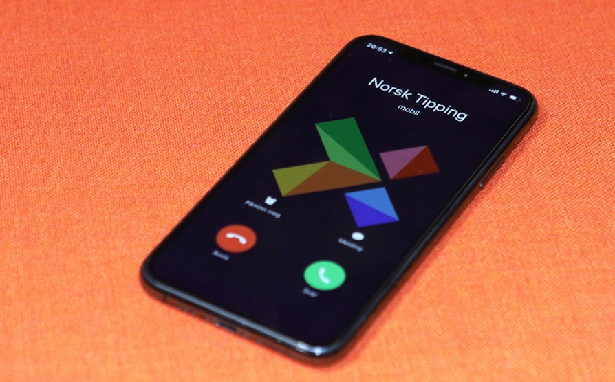 Mobiltelefon på oransje bakgrunn: Norsk Tipping ringer