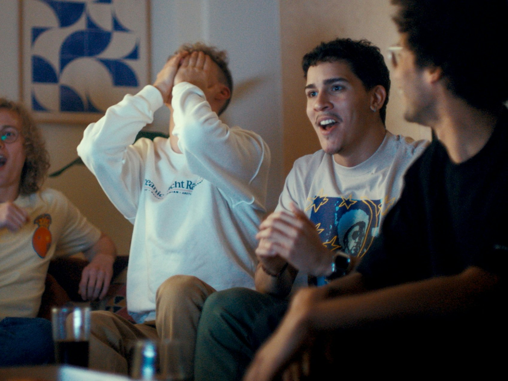 Illustrasjonsfoto av fire menn som reagerer på noe som skjer utenfor skjermen: to er overrasket, en skjuler ansiktet i hendene mens fjerdemann følger leende med