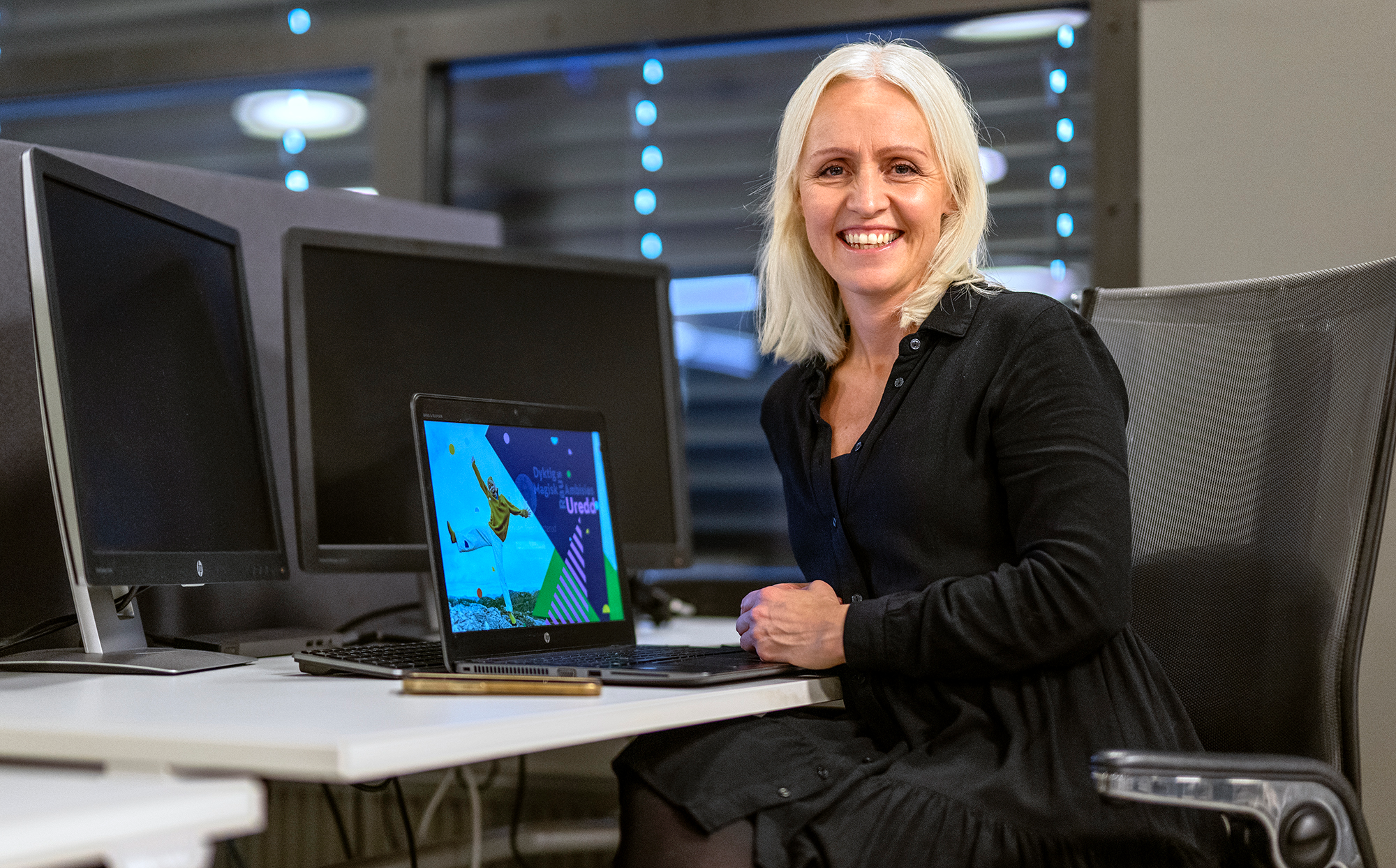Ingrid Rotherud Mathisen sitter i en sort kjole foran en kontorpult med laptop.