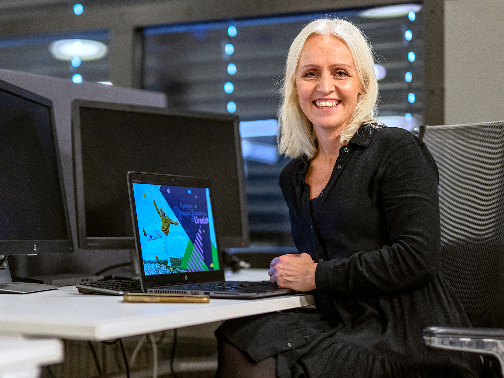 Ingrid Rotherud Mathisen sitter i en sort kjole foran en kontorpult med laptop.