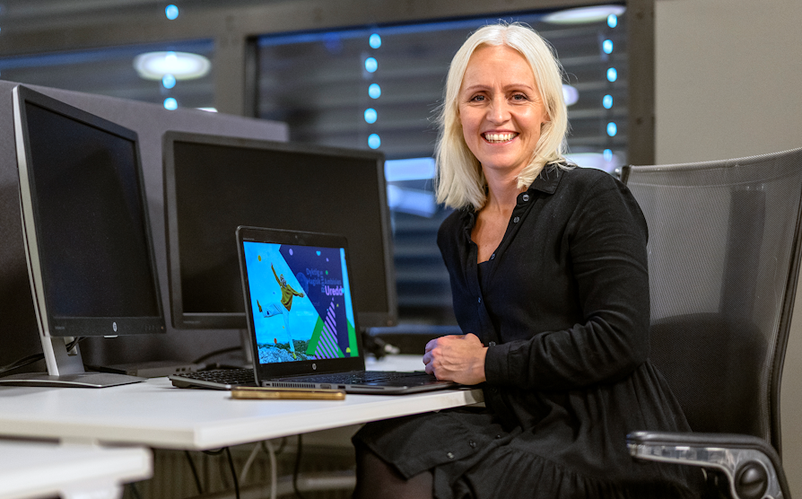Ingrid Rotherud Mathisen sitter i en sort kjole foran en kontorpult med laptop.